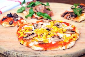 Grilled pizza on a wooden, circular cutting board.