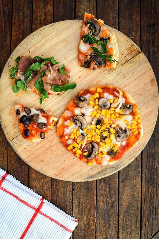 Grilled pizza on a wooden, circular cutting board.