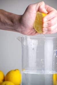 A woman's hand squeezing lemon into a tall pitcher of water.