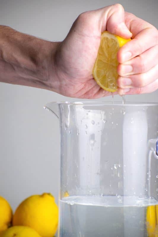A woman's hand squeezing lemon into a tall pitcher of water.