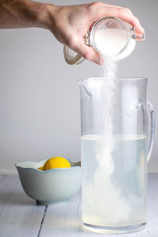 A tall pitcher of lemonade, a woman's hand pouring sugar in.