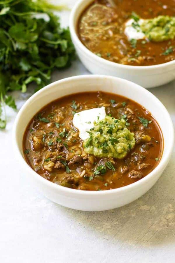 Salsa verde taco soup with a dallop of sour cream in a white bowl.