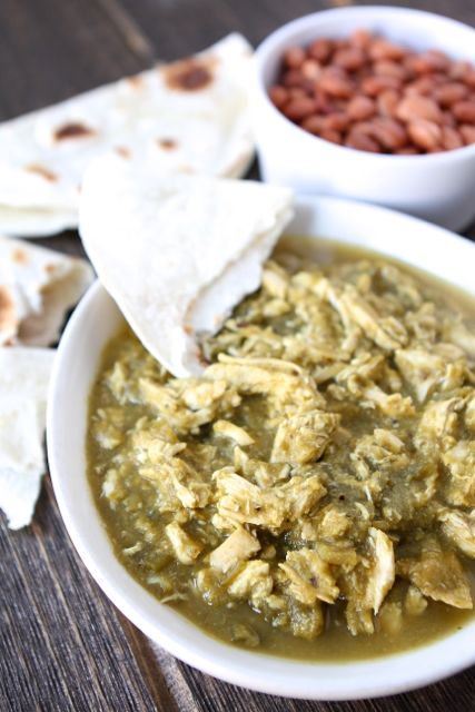 Slow cooker chicken chile verde in a white bowl with soft tortillas on the side.