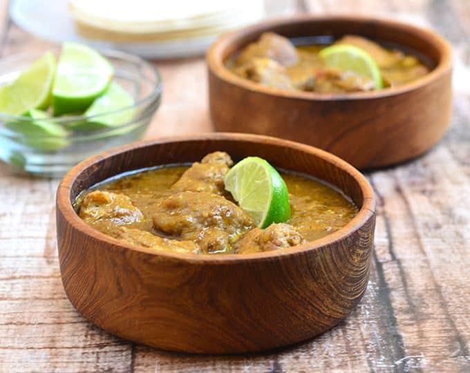 Pork chili verde in 2 wooden bowls with lime slice garnishes.