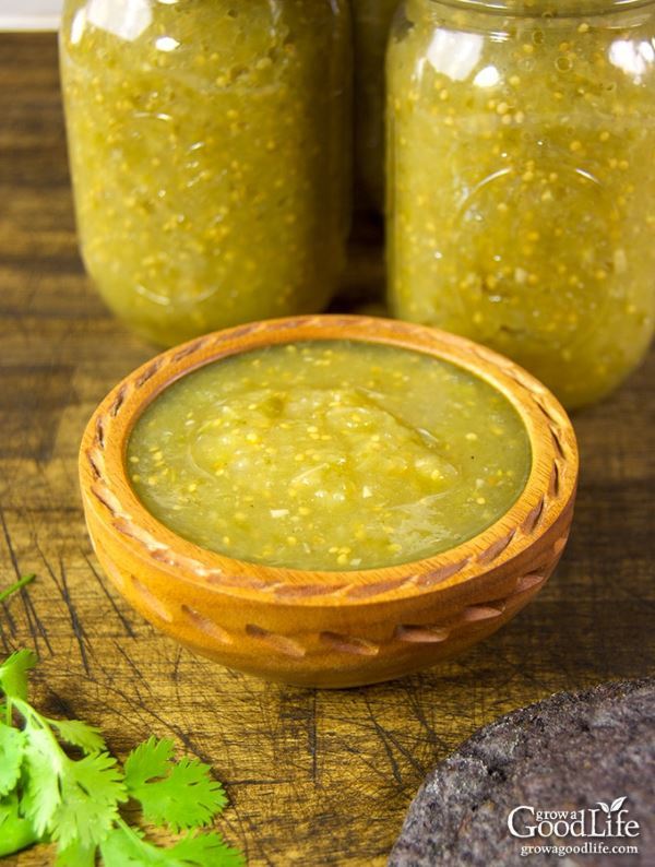 A wooden bowl of tomatillo salsa and 2 canning jars in the back.