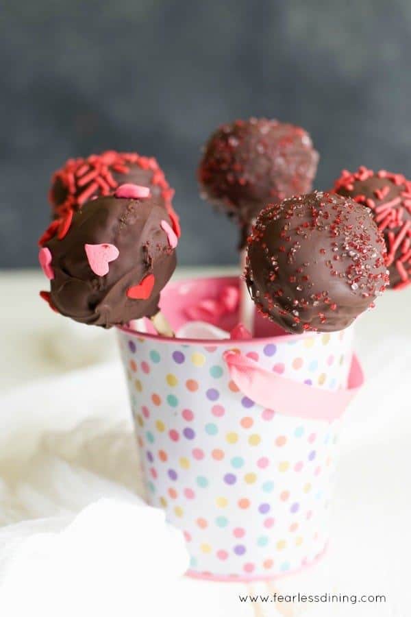 Gluten free chocolate cake pops with heart sprinkles in a small polka dot pail.