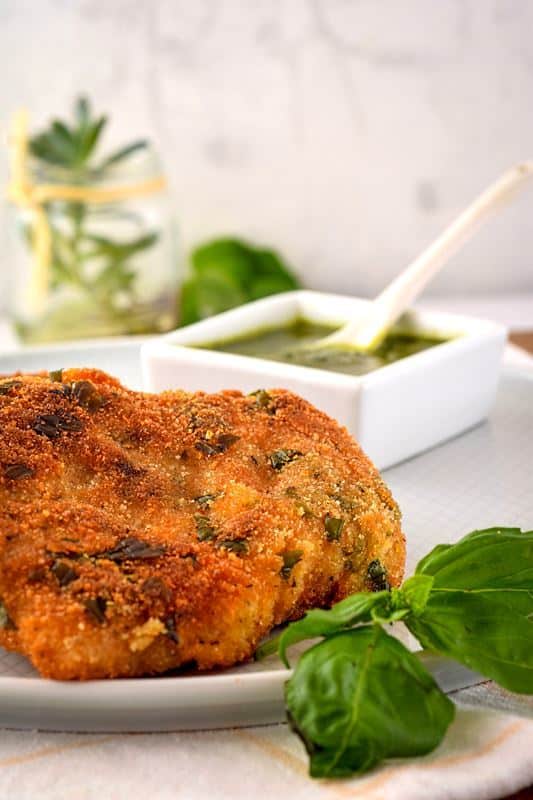 Electric skillet fried fish on a plate with basil pesto in the background.