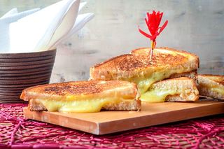Electric skillet grilled cheese sandwiches on a cutting board over a pink doiley.