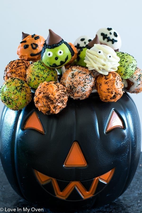 Witch, ghost and green and orange cake pops for Halloween in a black plastic jack o lantern.