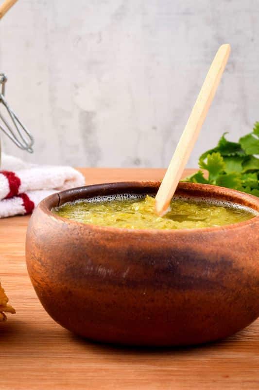 How to Make Tomatillo Salsa_12 A wooden bowl of tomatillo salsa, cilantro in the background.