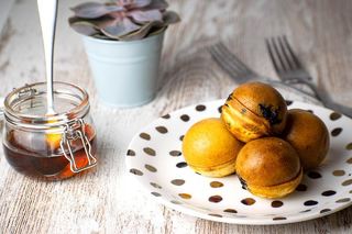 Pancake cake pops on a white plate with polka dots, a jar of maple syrup in the background.