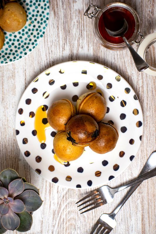 Pancake cake popPancake cake pops covered in maple syrup on a white plate with polka dots.s on a white plate with polka dots, a jar of maple syrup in the background.