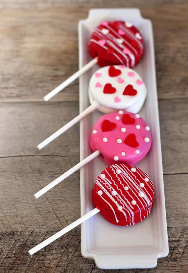 Oreo cake pops covered in red, white and pink icing, lined up on a porcelain dish.