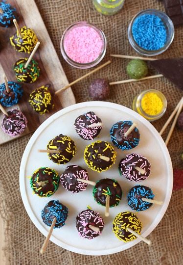 Rainbow cake pops with chocolate coating and colorful sprinkles on a tray.