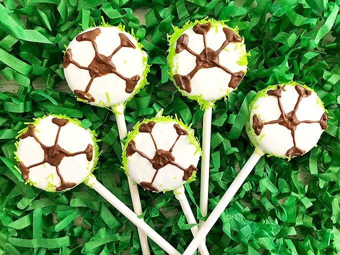 Soccer oreo cake pops on green shredded paper.