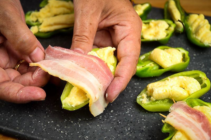How to Grill Jalapeño Poppers_8 A hand wrapping a jalapeno popper with raw bacon on a cutting board.
