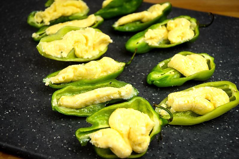 Raw jalapenos sliced in half with cheese in them on a cutting board.