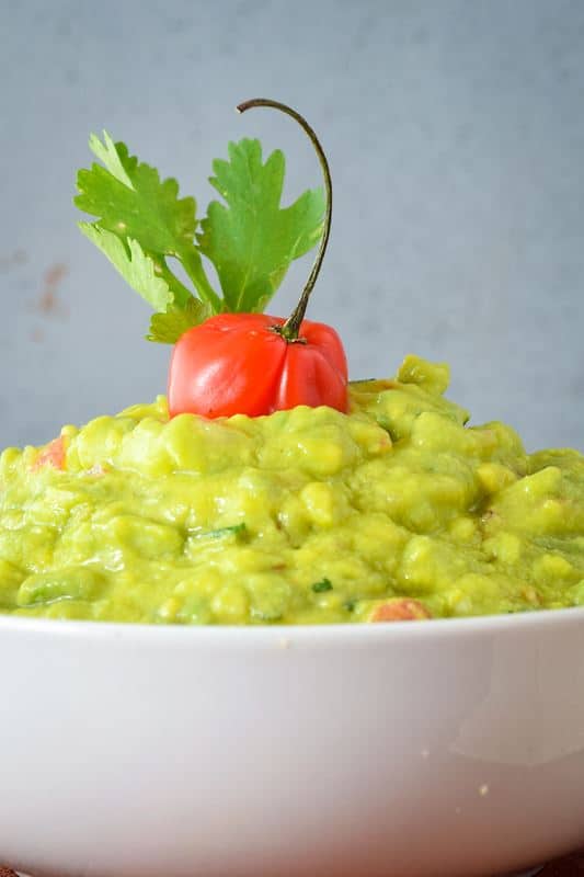 A bowl of guacamole with cilantro and a pepper.