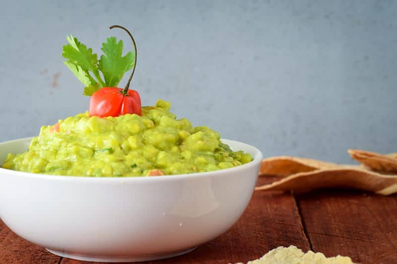 A bowl of guacamole with cilantro and a pepper. Dark reddish-brown background.