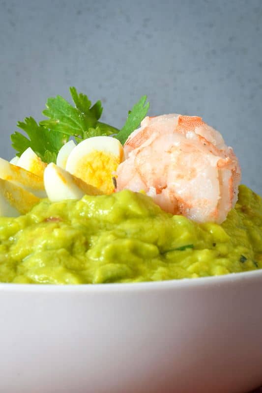 A bowl of guacamole with sliced quail eggs and prawns.