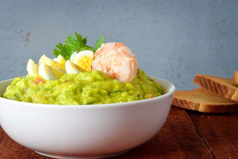 A bowl of guacamole with sliced quail eggs and prawns.