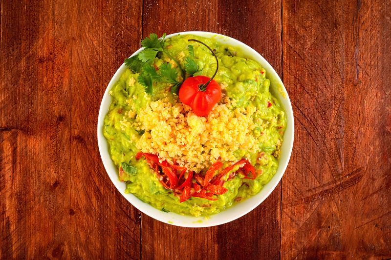 A bowl of guacamole with a chili pepper, cilantro, Mexican seasoning and cheddar cheese.