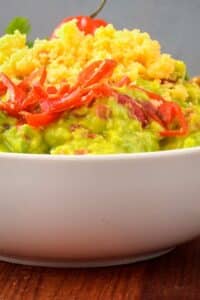 A bowl of guacamole with a chili pepper, cilantro, Mexican seasoning and cheddar cheese.