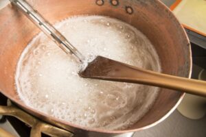 Large pot of maple syrup boiling with candy thermometer and wooden spoon.