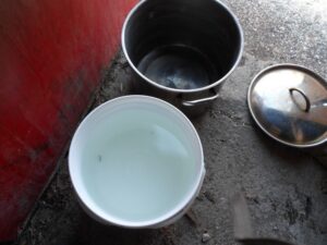 A pail and a large pot on concrete floor.