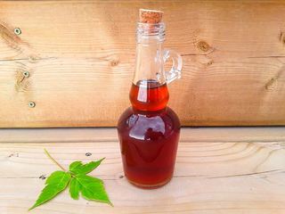 Maple syrup in a glass bottle with a maple leaf on the side, wood background.