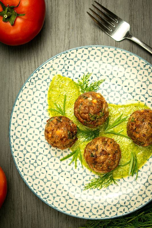 Mediterranean meatballs on a plate with pesto, tomatoes and dill on the side, grey wood background.