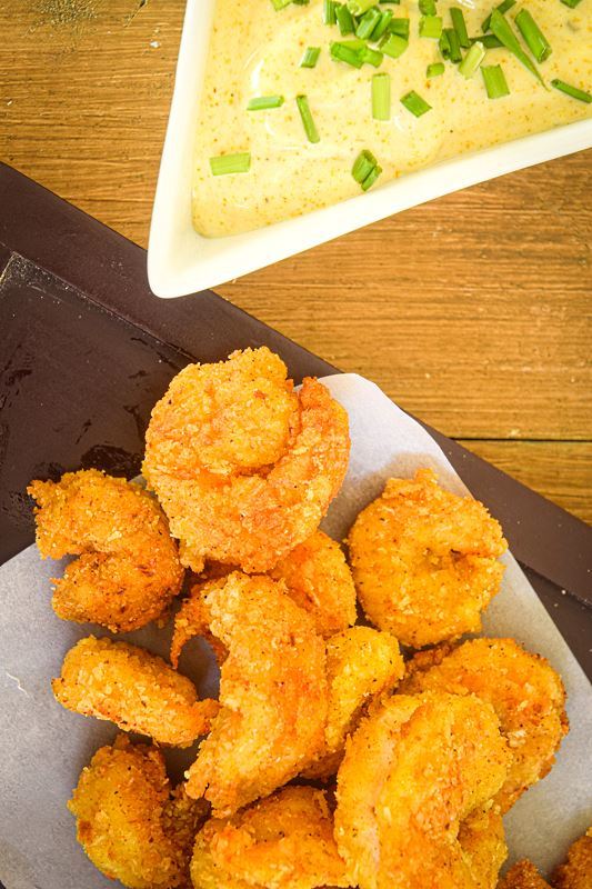 Fried coconut shrimp on a brown serving plate, curry dip on the side.