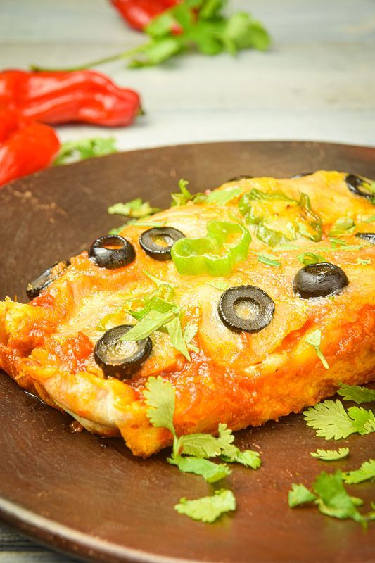 Electric Skillet Chicken Enchiladas on a wooden plate, chilies in the background.