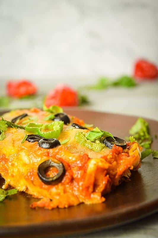 Electric Skillet Chicken Enchiladas on a wooden plate, chilies in the background.