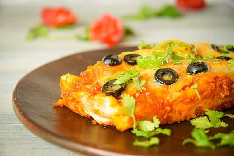 Electric Skillet Chicken Enchiladas on a wooden plate, chilies in the background.