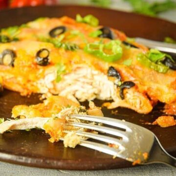 Electric Skillet Chicken Enchiladas on a wooden plate, chilies in the background.