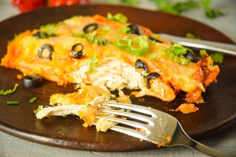 Electric Skillet Chicken Enchiladas on a wooden plate, chilies in the background.