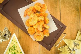 Fried coconut shrimp on a black serving tray, curry dip on the side.