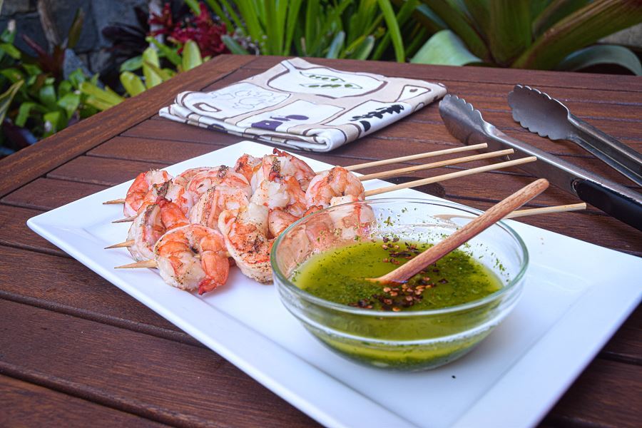 How to Grill Jumbo Shrimp _19 Grilled shrimp skewers on white plate with a bowl of chimichurri sauce.