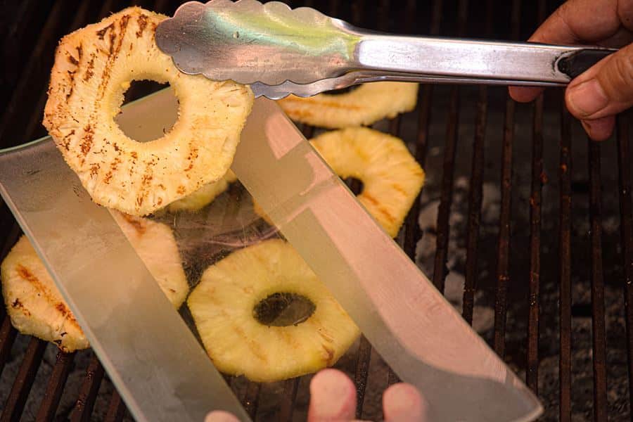 How to Grill Pineapple Slices_10 Pineapple slices on the grill, being transferred to a glass plate.