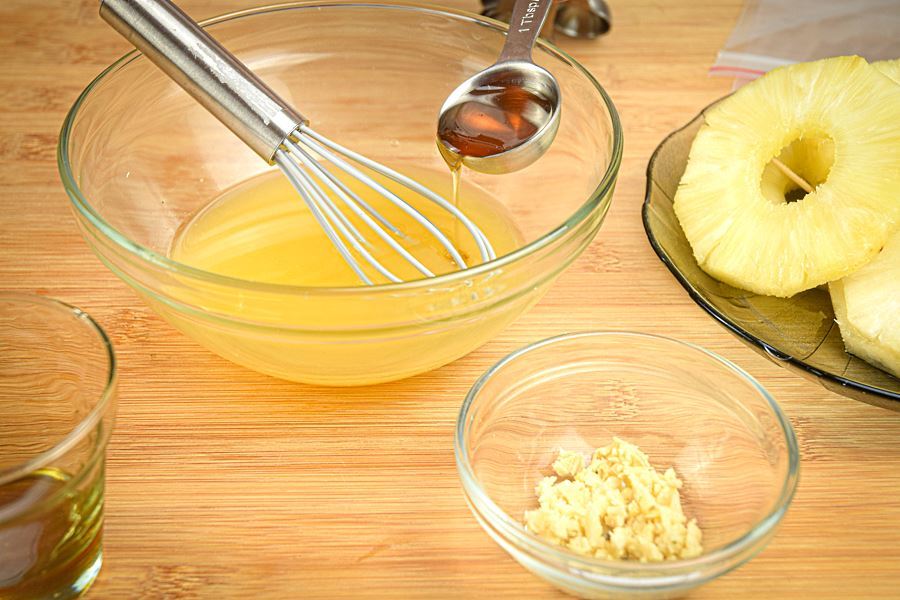 How to Grill Pineapple Slices_2 Honey being added to bowl of orange juice with a measuring spoon.