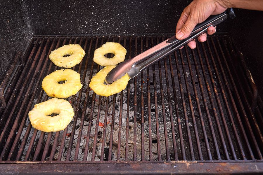 How to Grill Pineapple Slices_7 Pineapple slices on the grill, hand with tongs.