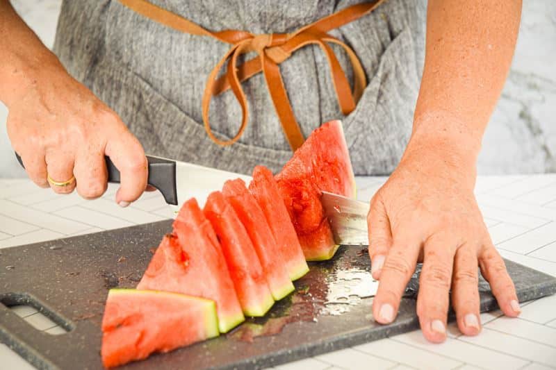 A woman slicing a watermelon into wedges.