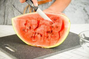 A woman making vertical slices into a watermelon.