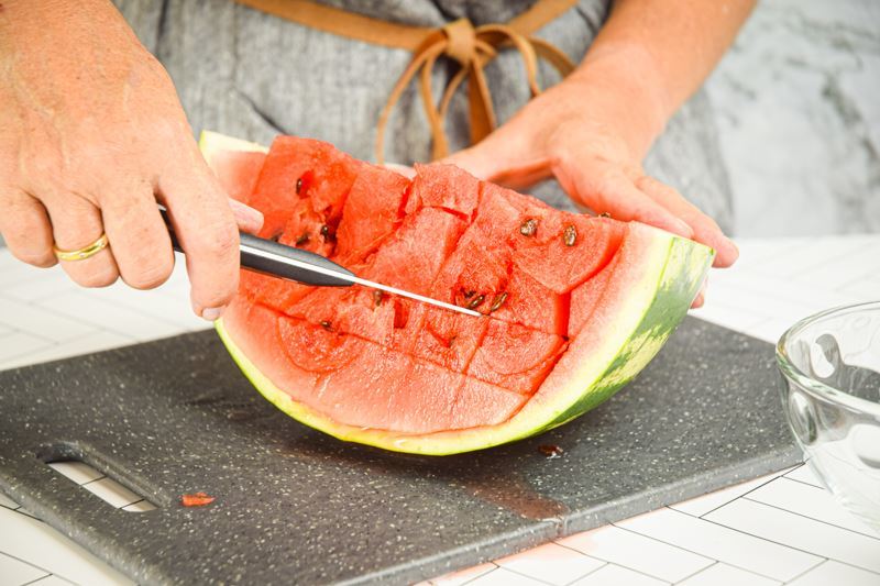 A woman making horizontal slices into a watermelon.