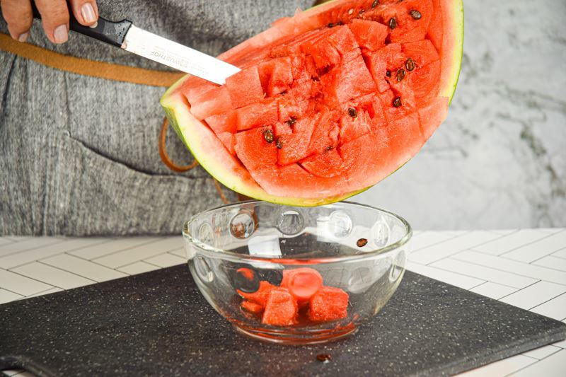 A woman cutting a watermelon into cubes.
