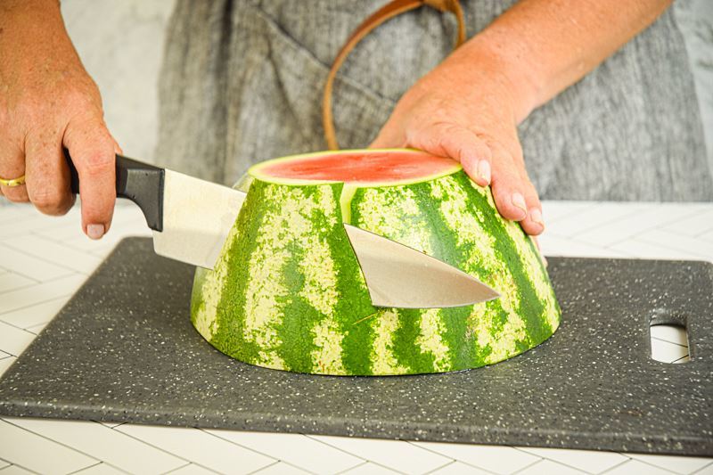 A woman slicing off watermelon rind.