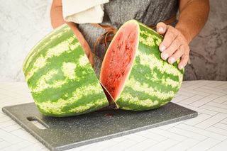 A woman slicing a knife into a large watermelon.