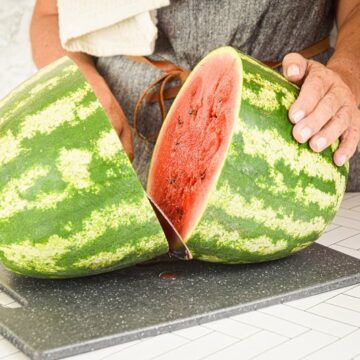 A woman slicing a knife into a large watermelon.