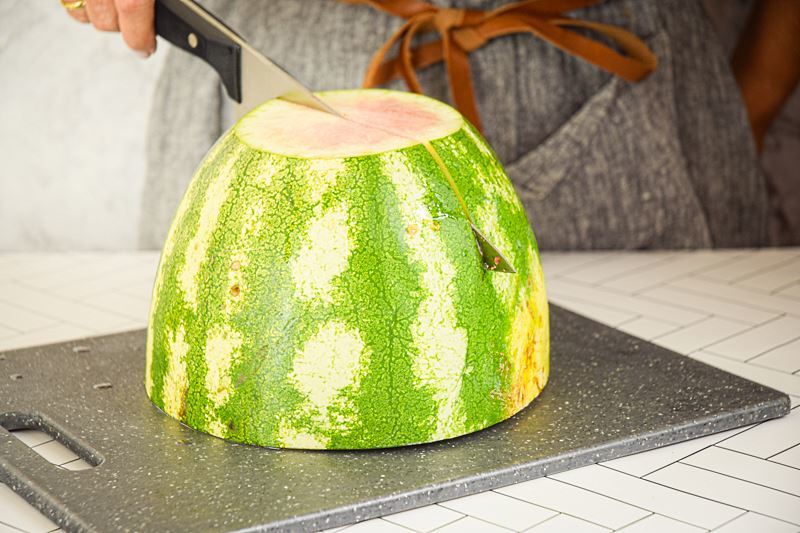 A woman quartering a large watermelon on a cutting board.